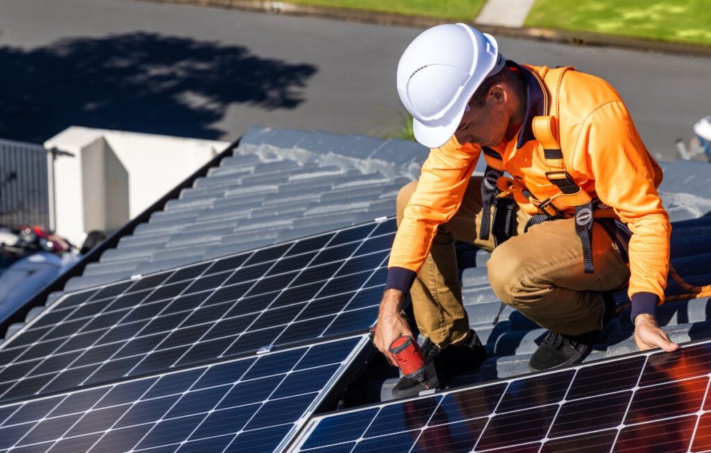 Technician in hard hat installing solar panels on rooftop