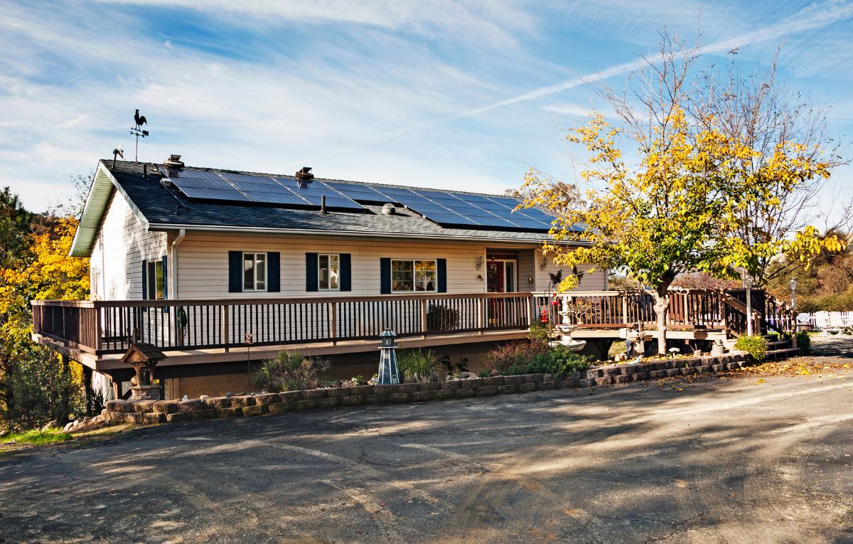 House with rooftop solar panels in a rural setting, illustrating solar battery maintenance for New York State Solar Farm