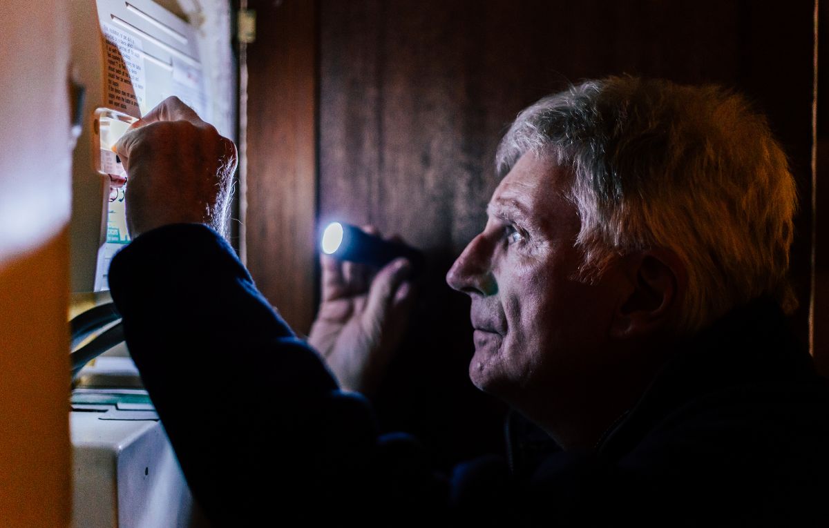 Man using a flashlight to check his electrical panel during a power outage