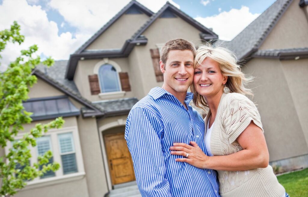 Couple standing together and smiling in front of their home, representing homeowners learning about battery storage warranties