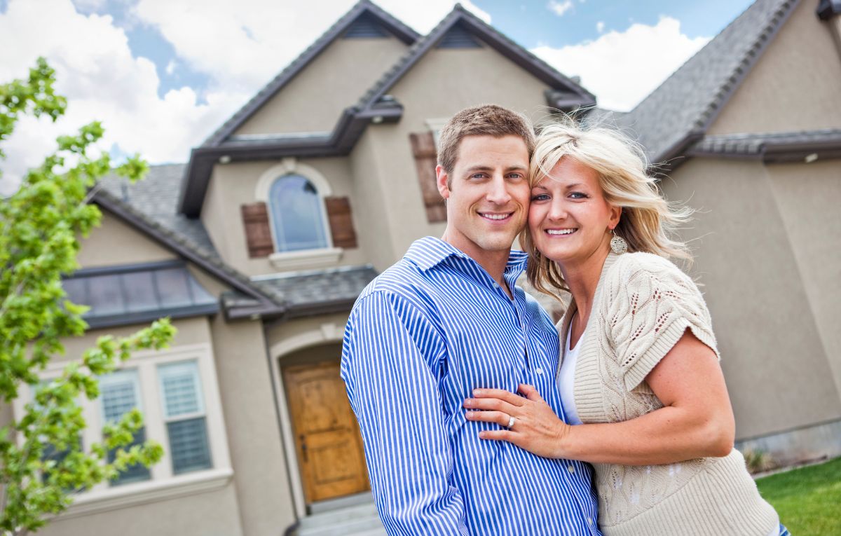 Couple standing together and smiling in front of their home, representing homeowners learning about battery storage warranties