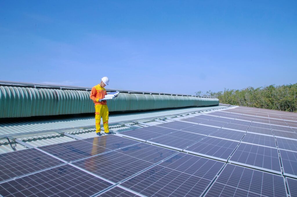 Solar technician in safety gear reviewing plans on a commercial rooftop after a solar site assessment.