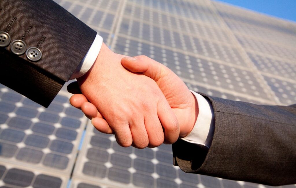 Business handshake in front of solar panels representing solar installer services